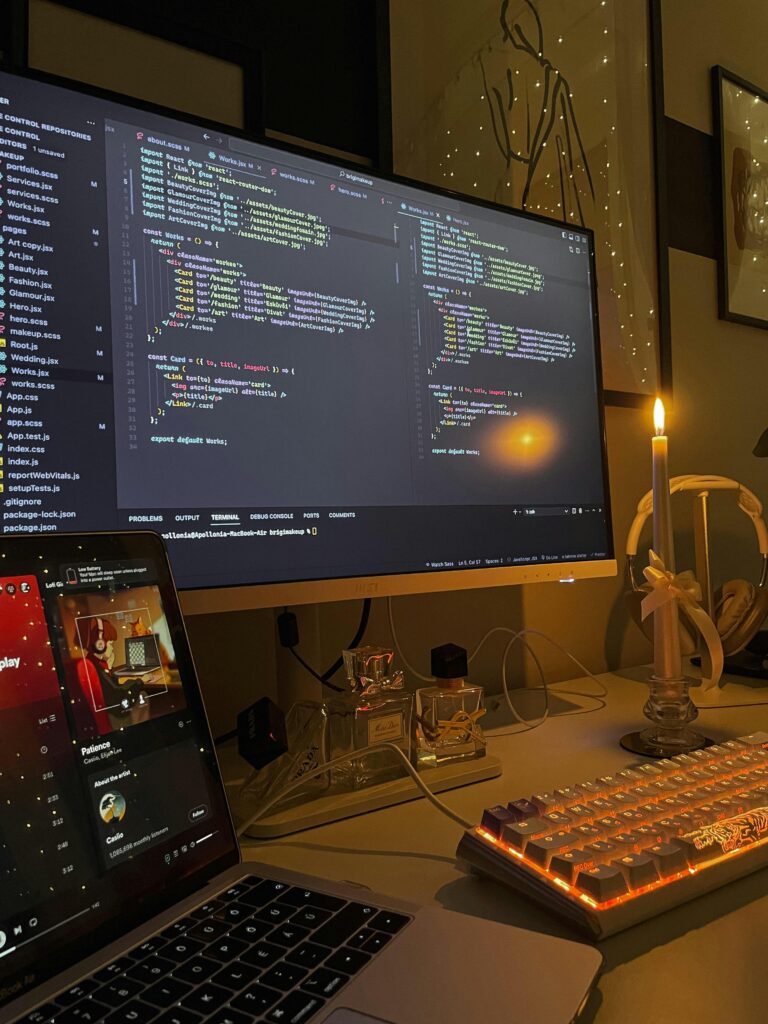 A tech workspace featuring a lit candle and a computer screen displaying code, creating a warm coding environment.